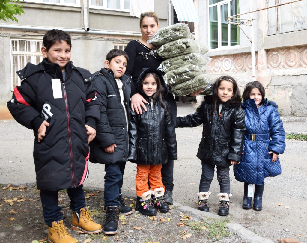 A woman and five children; the woman is carrying blankets, the children are wearing warm coats and shoes